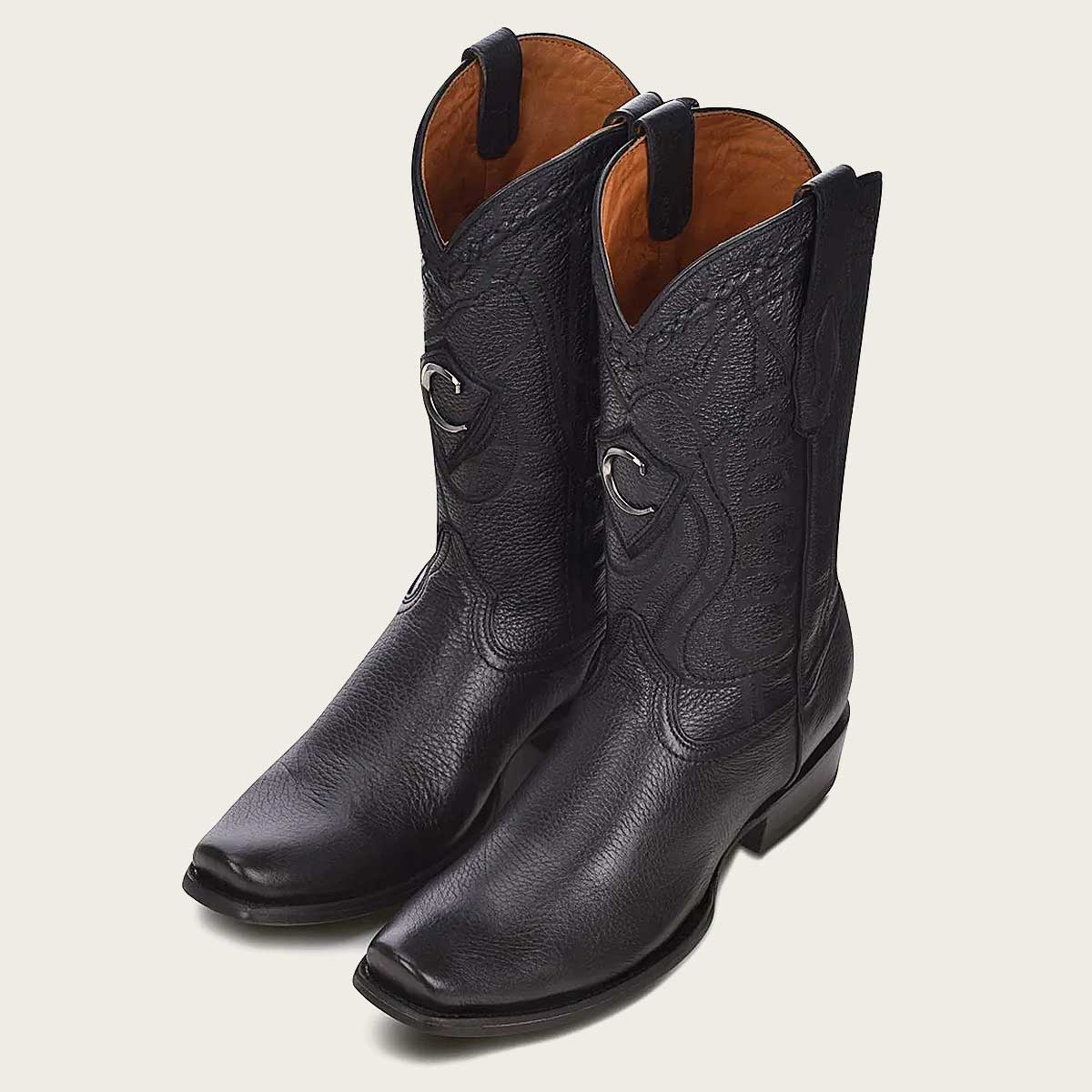 Stylish black leather boot with intricate engraving and a metallic monogram accent.
